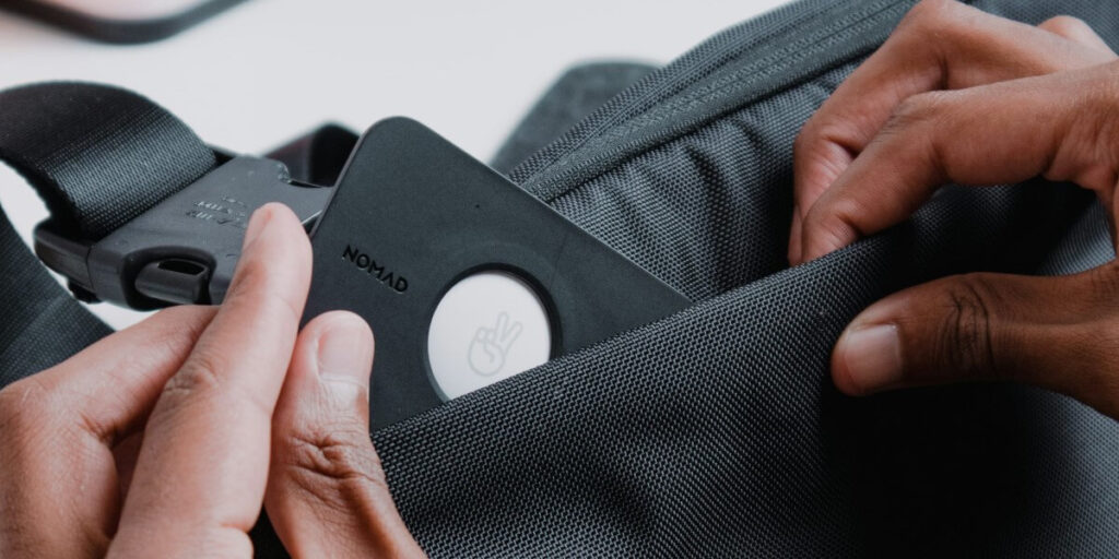 Hands placing a GPS tracker inside a black bag, demonstrating the discreet use of tracking technology.