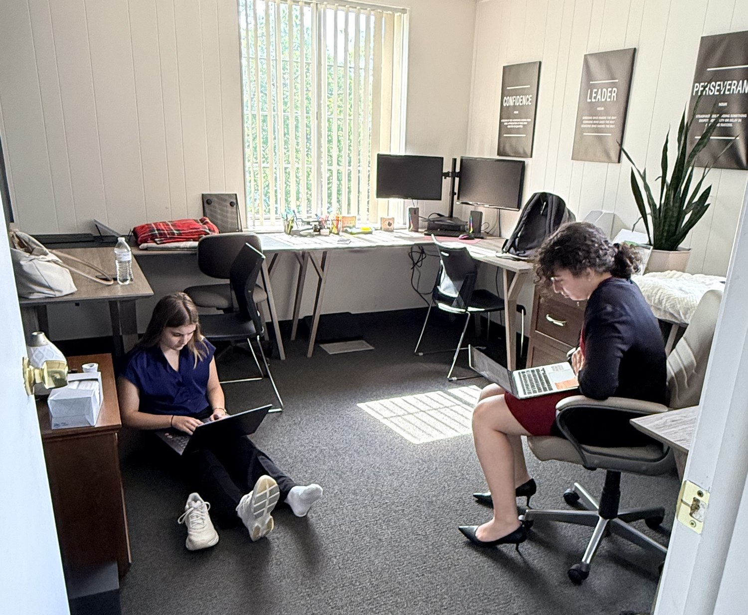 Two PPIC interns working on laptops, one seated on the office floor